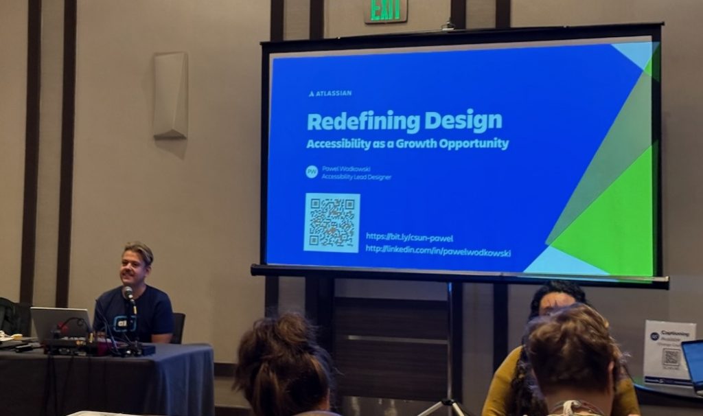 Powell seated behind his laptop, in front of the presenting screen with this title slide showing.