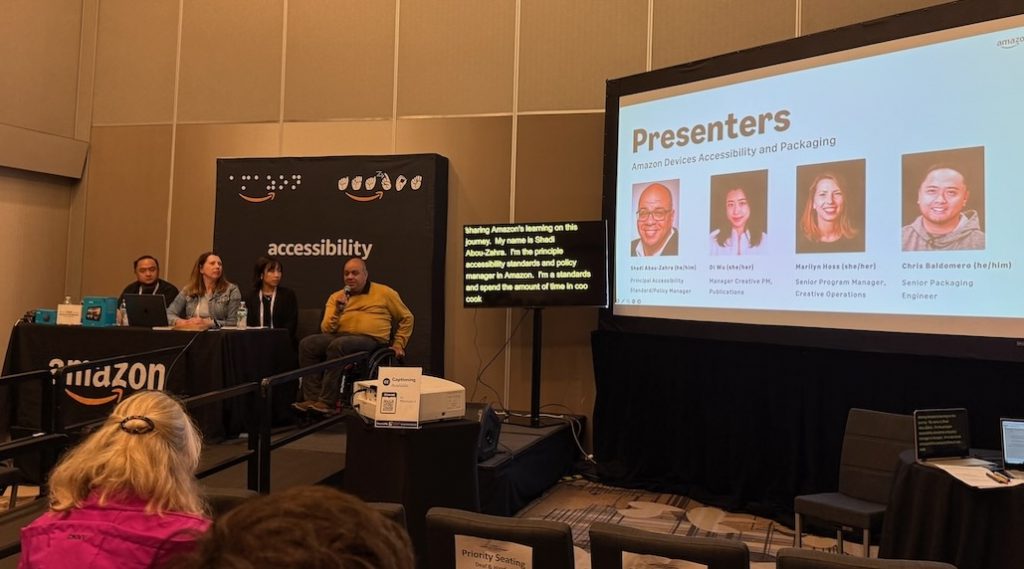 The 4 speakers lined up behind a table, and on screen with their introduction slide.